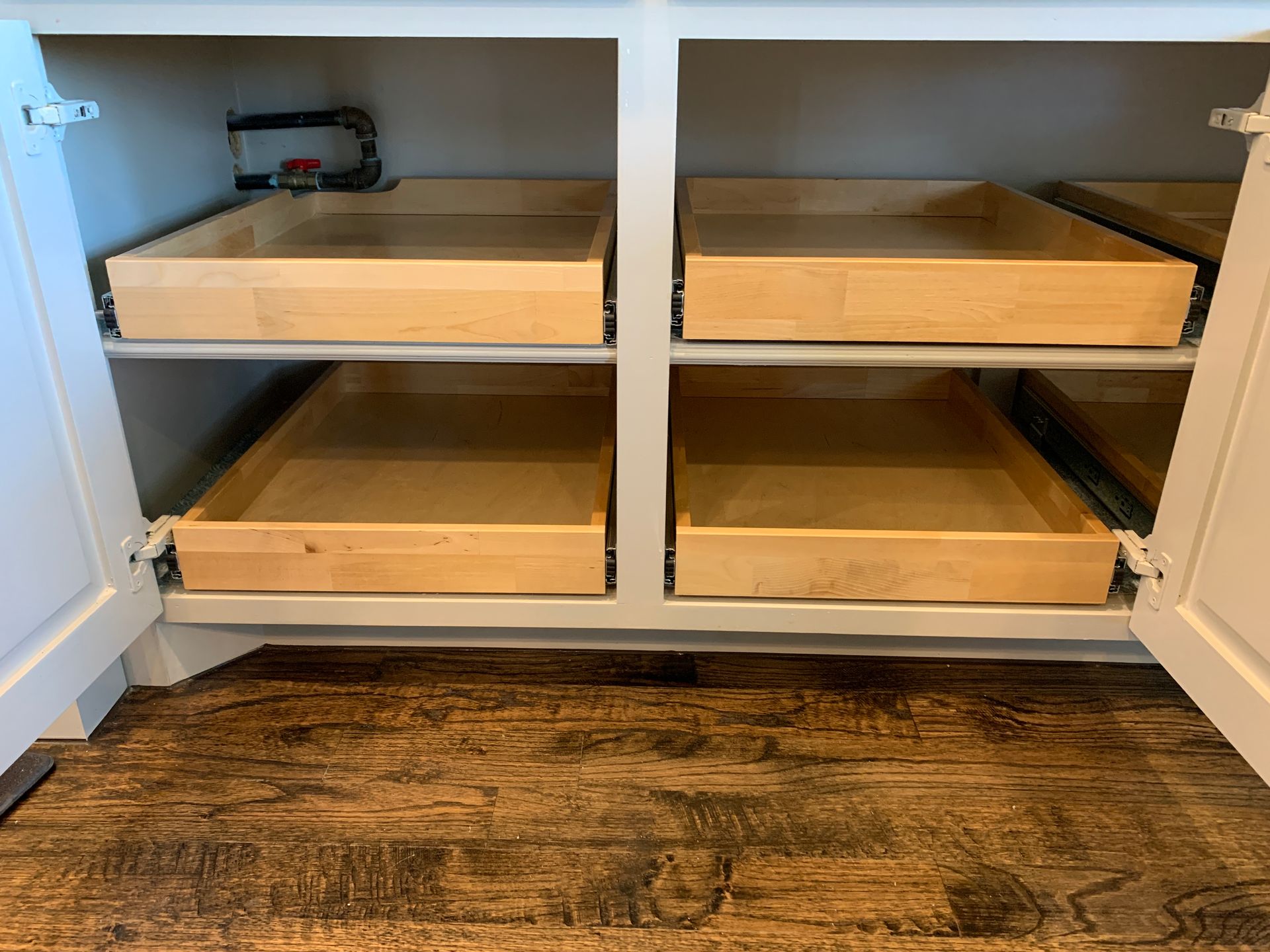 Open white kitchen cabinet with four pull-out wooden shelves. Brown wooden flooring in front.