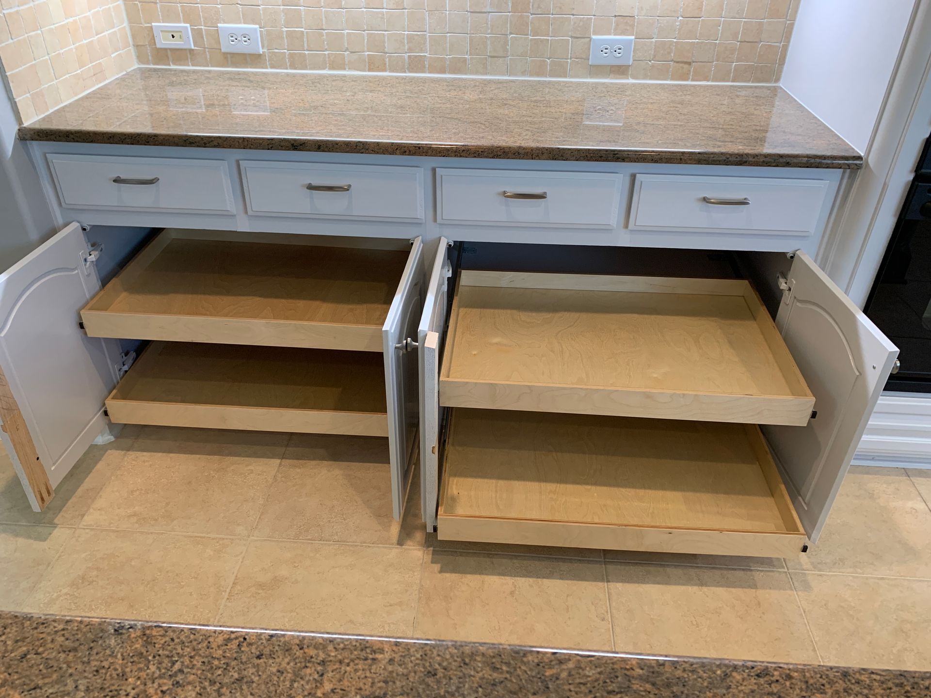 White kitchen cabinets with pull-out shelves. Granite countertop, tan tile backsplash, and light-colored flooring.