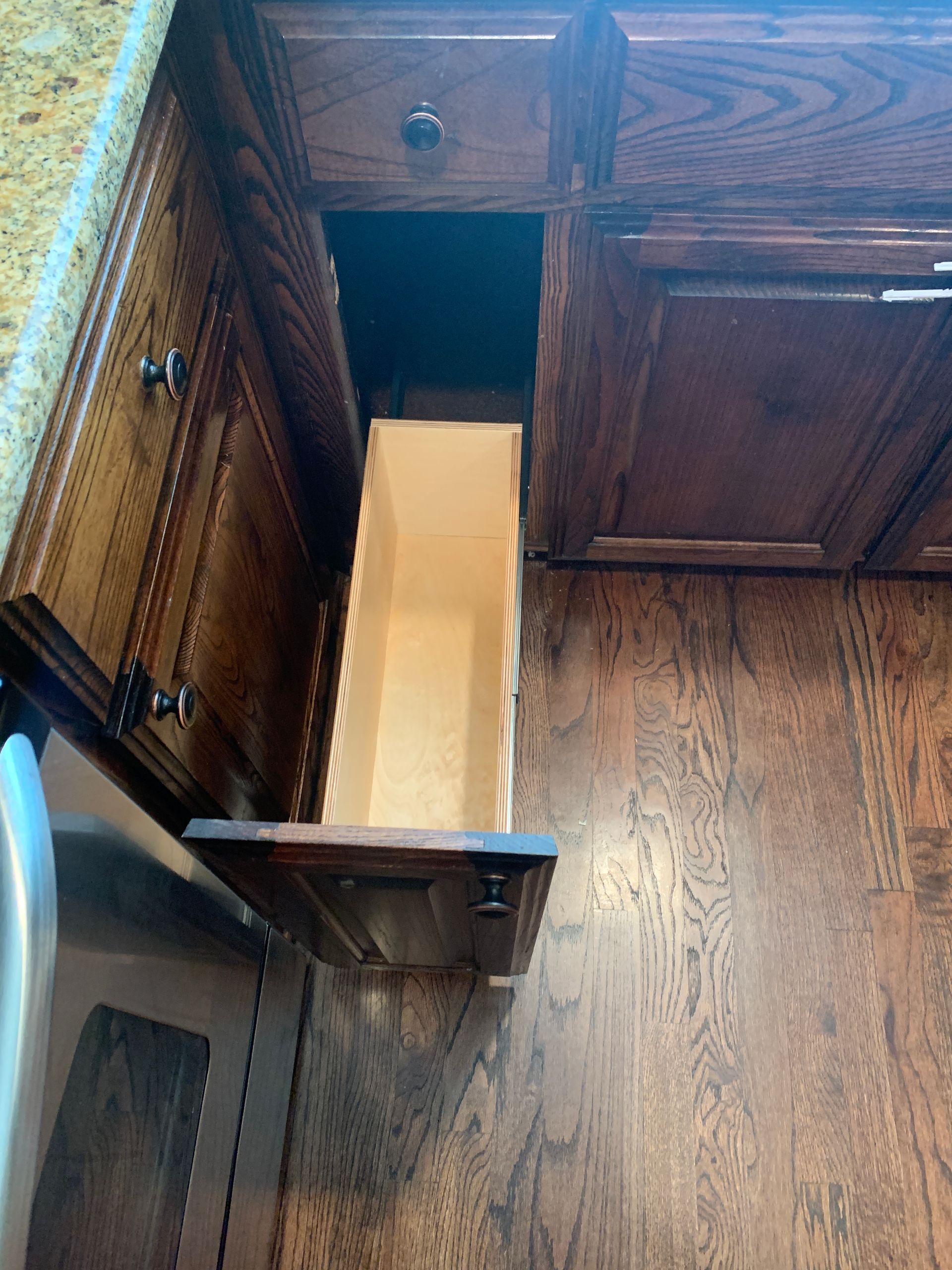 Open kitchen cabinet with a tall, narrow pull-out drawer. Dark wood cabinets and flooring.