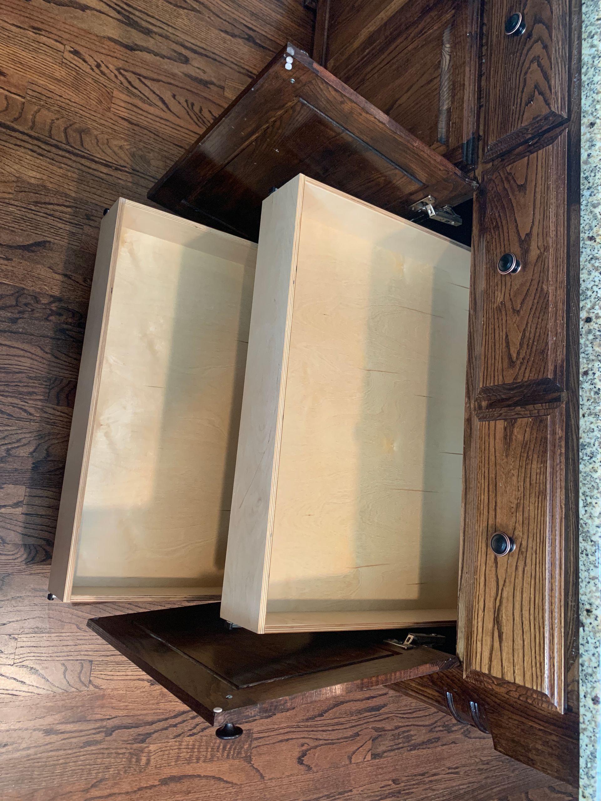 Two open wooden kitchen drawers in a corner cabinet; showing a dark wood finish and light wood interiors.