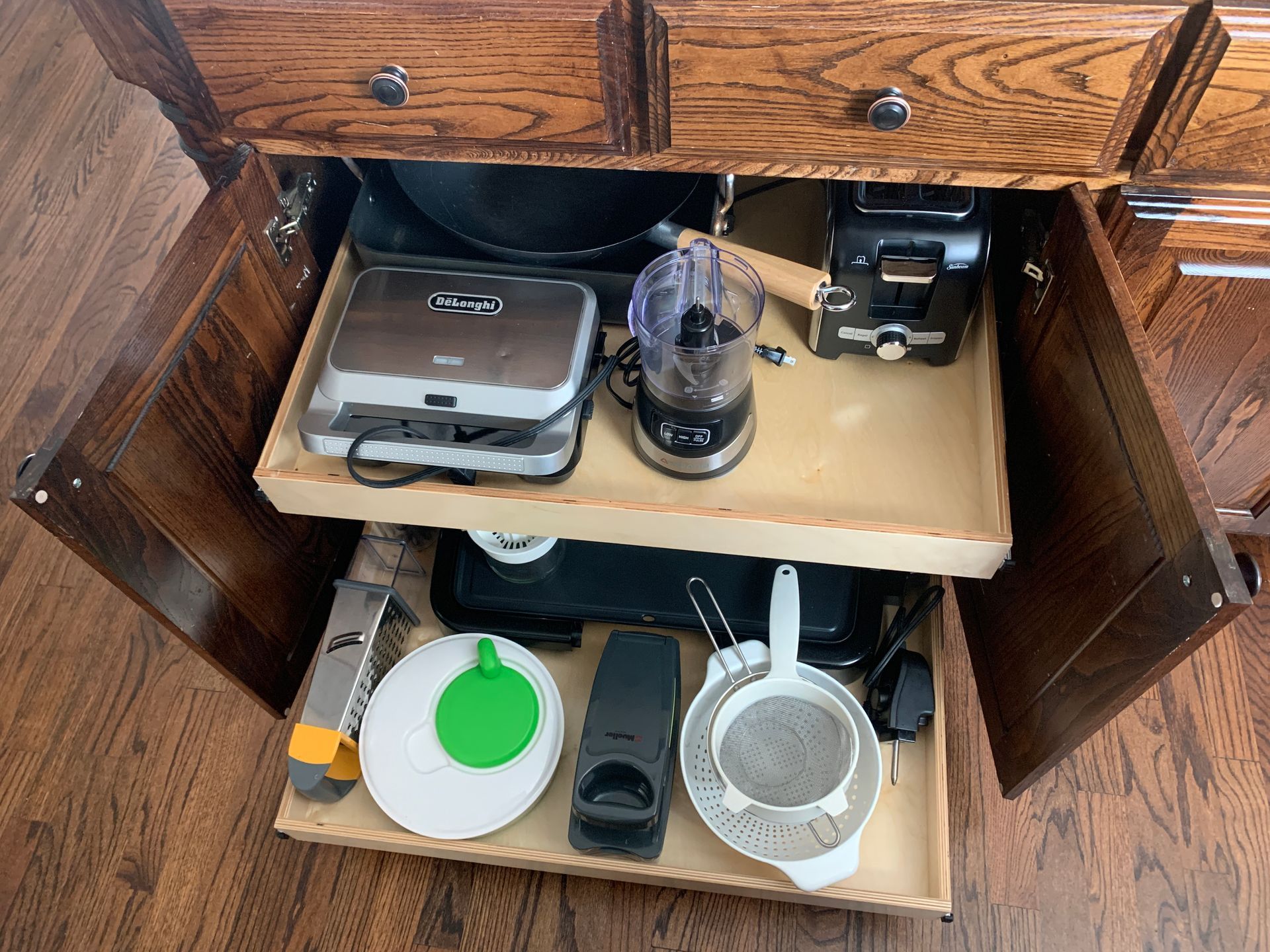 Kitchen cabinet with pull-out shelves holding small appliances and cooking tools in a wooden cabinet.