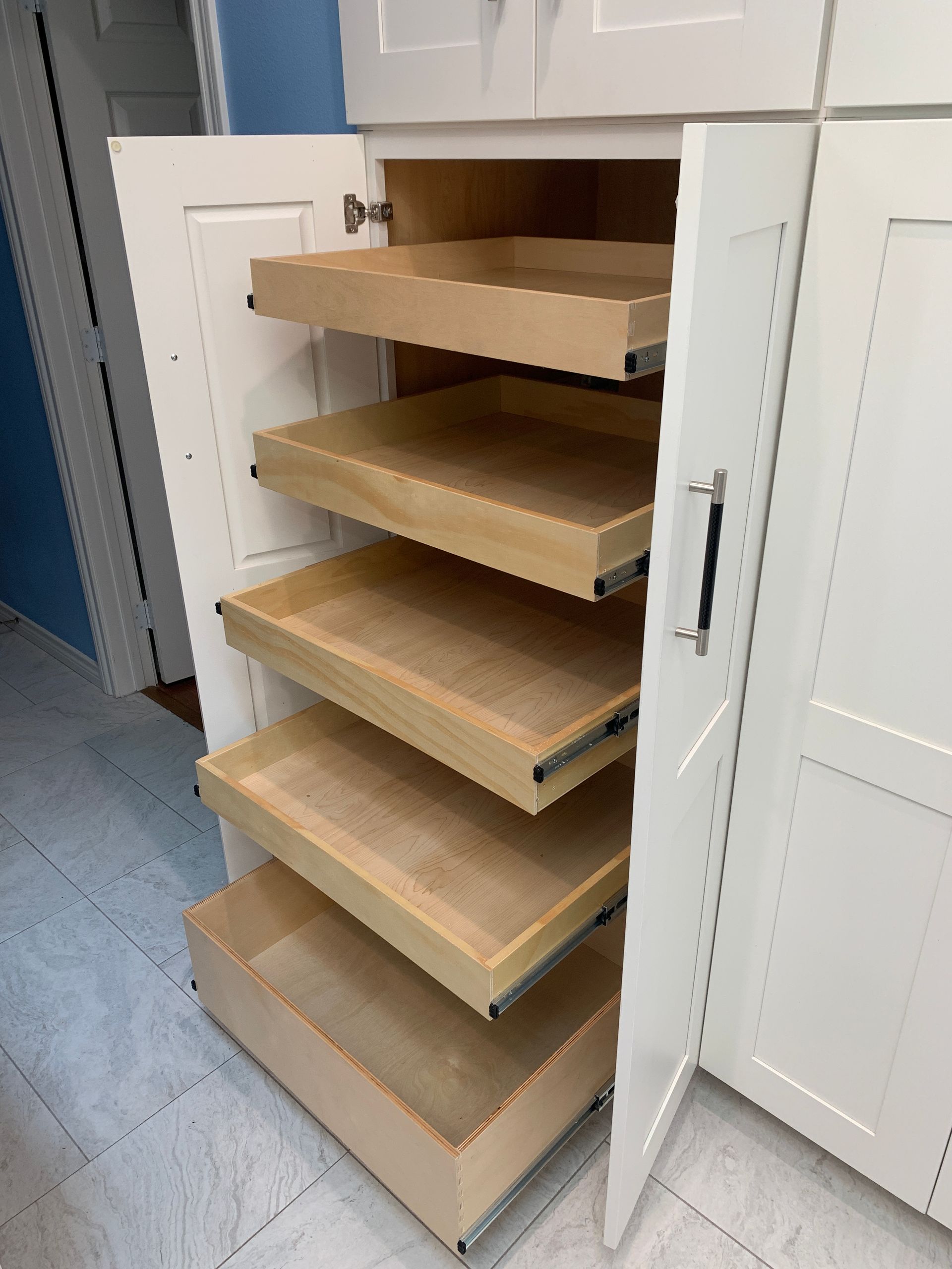 White pantry cabinet with pull-out drawers, open. Drawers are light wood, cabinet is white.