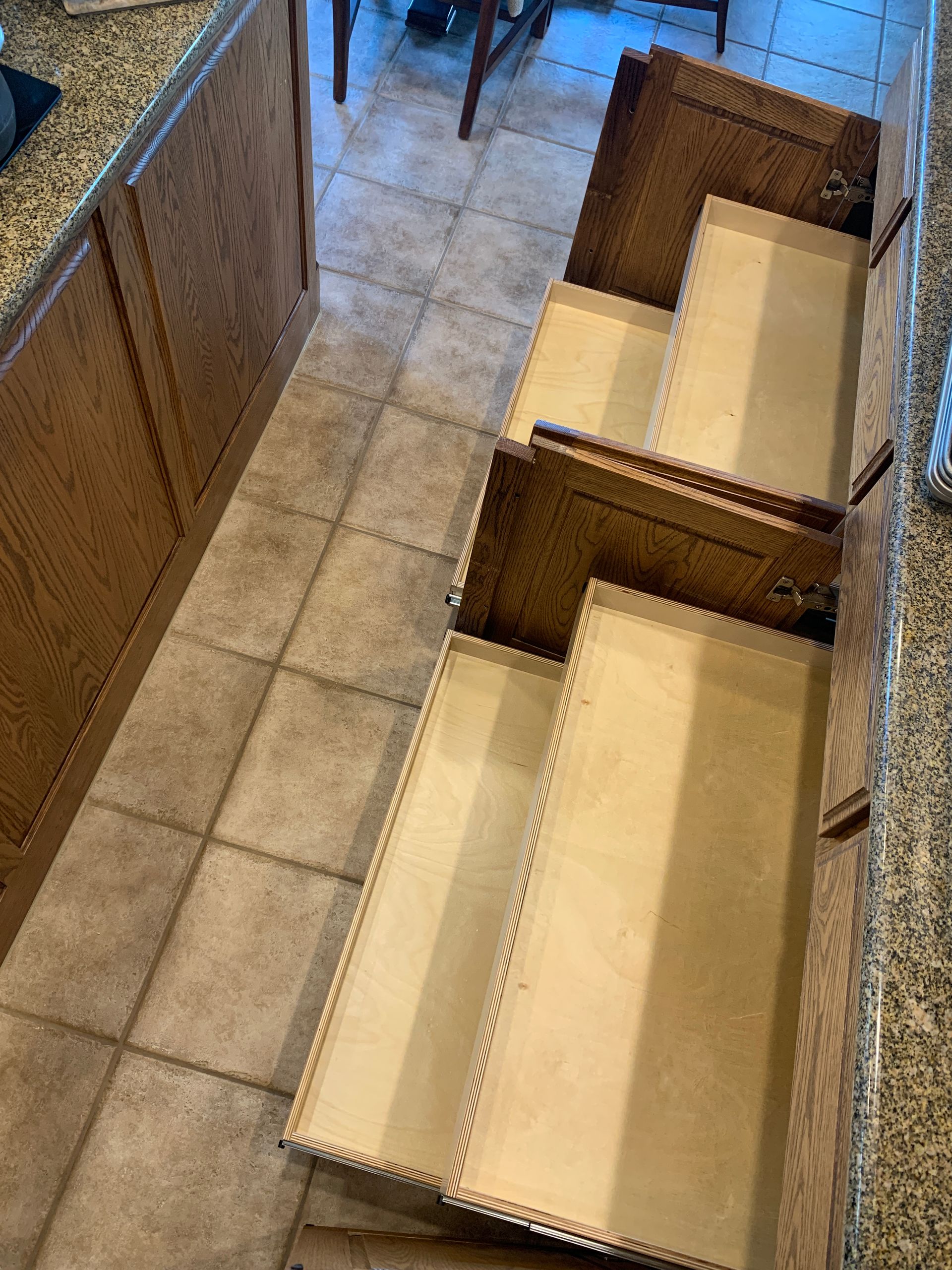 Open kitchen drawers in oak cabinets on a tile floor.