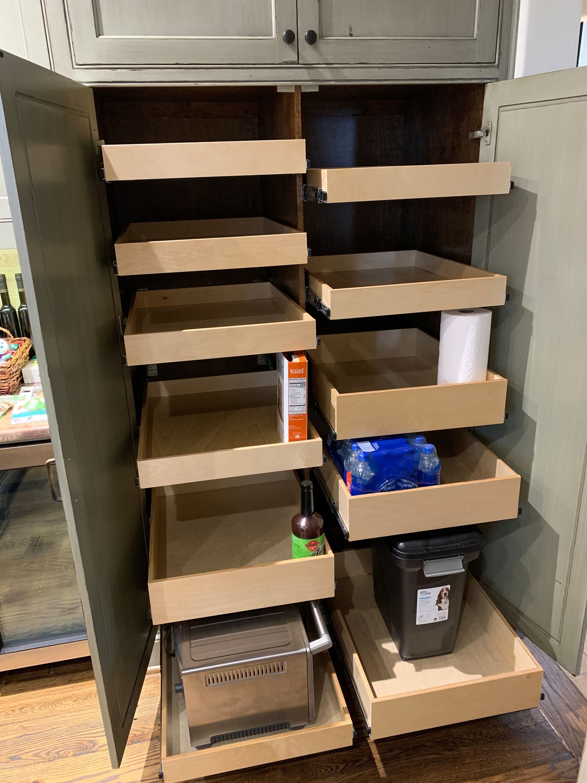 Tall pantry cabinet with pull-out drawers and shelves, holding food, toaster, and trash can.