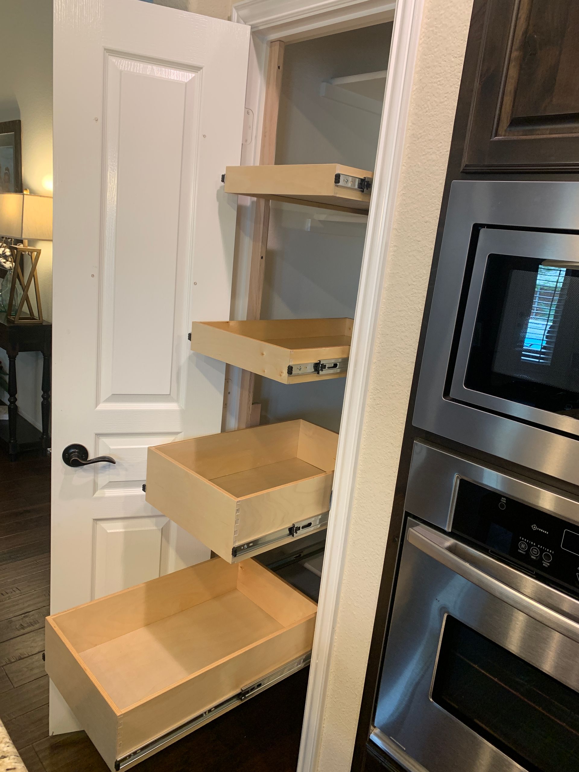 Pull-out shelves inside pantry. Wooden drawers on tracks, built into a narrow closet next to a microwave and oven.
