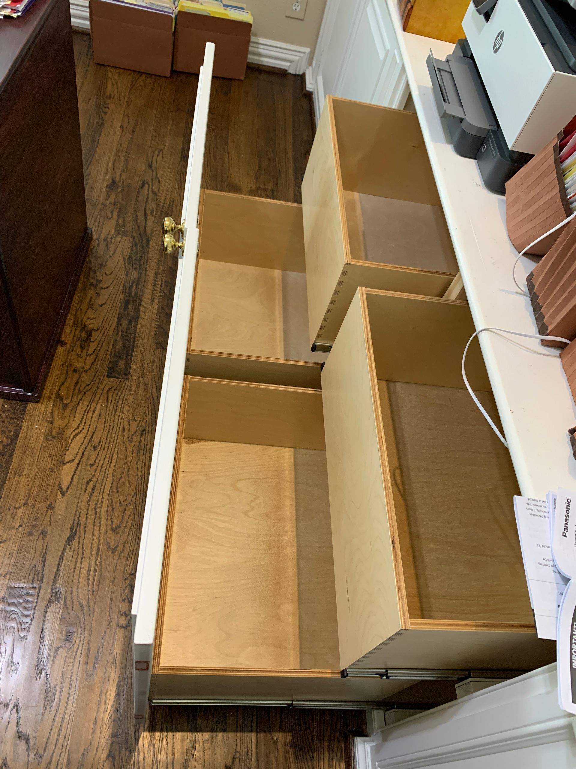 Open white drawers in a wood-paneled cabinet, viewed from above. The drawers are empty and wooden.