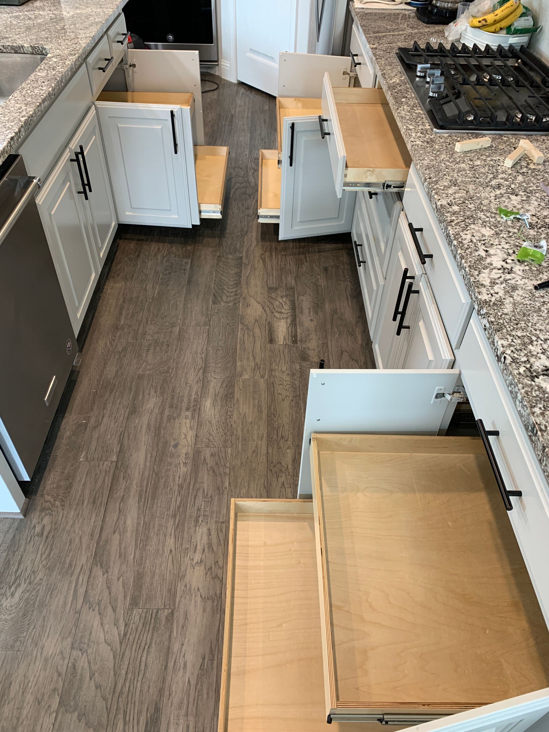 Kitchen cabinets with open drawers, drawers pulled out, wood floor, granite countertop, stove.