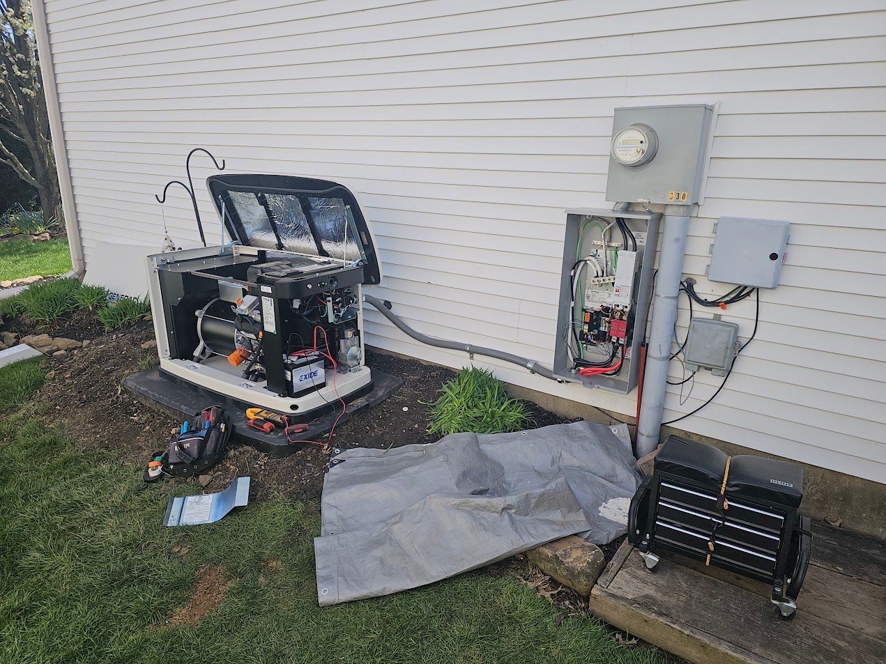 A generator being worked on next to a house with an open electrical box.