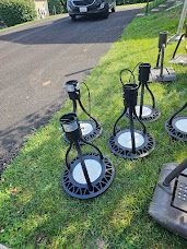 Several black event lights on green grass next to a paved driveway, car parked in the background.