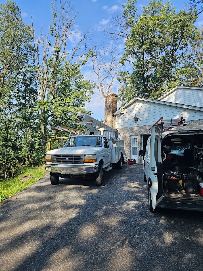 White service truck and van parked at a white stone house, a worker by the open van door.