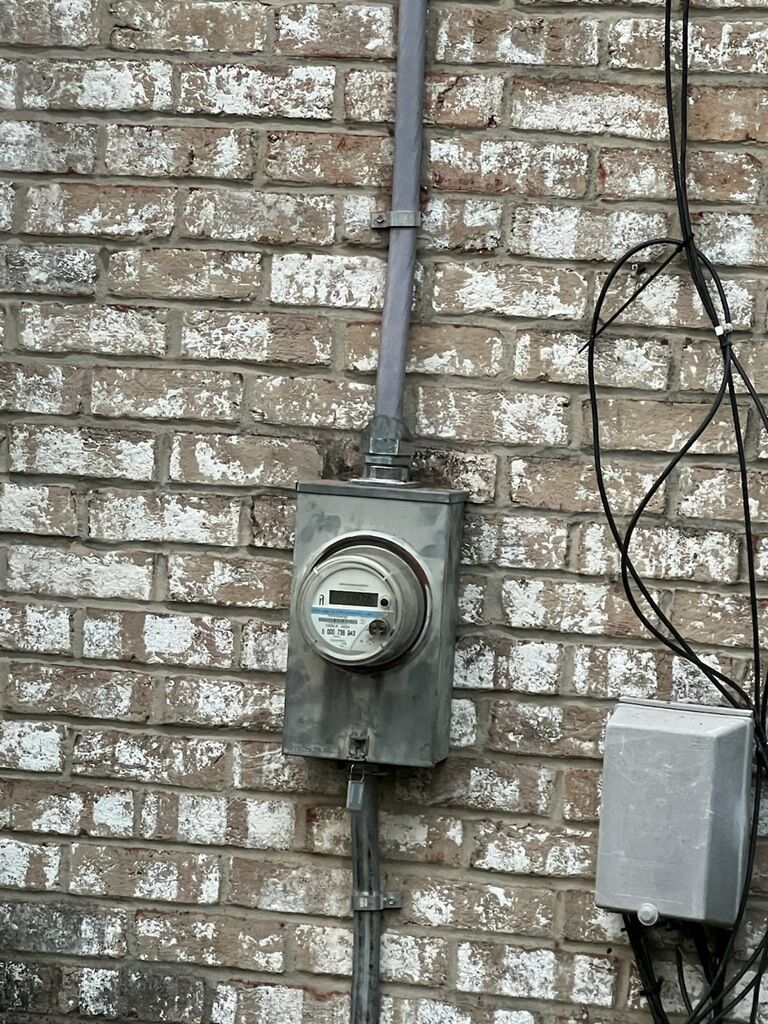 Electric meter box on a brick wall, with conduit and attached gray box.