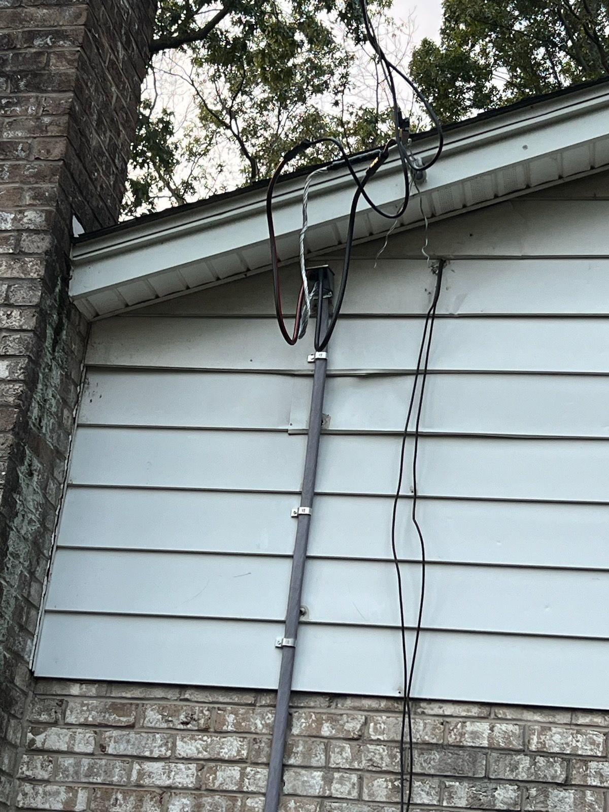 Gray pole with wires attached to the side of a house.
