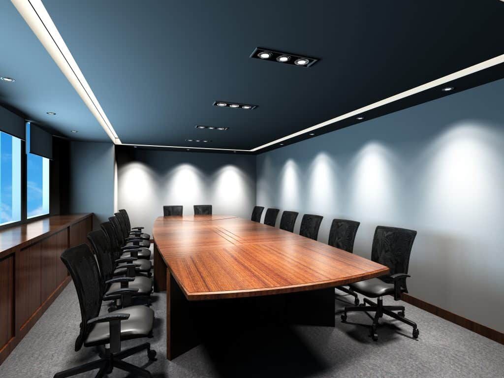 Modern conference room with long wooden table, black chairs, and blue walls.