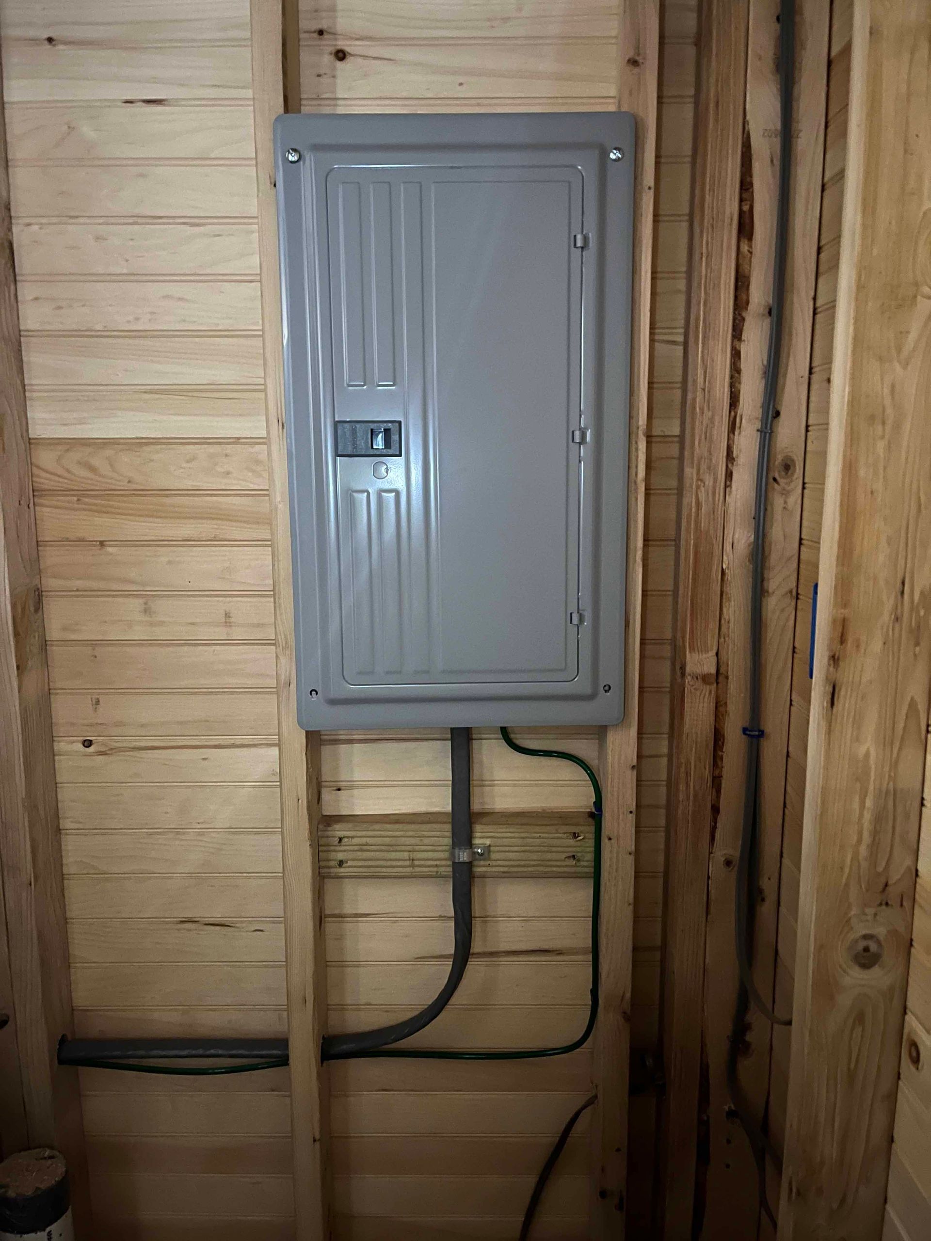 A gray electrical box is hanging on a wooden wall.