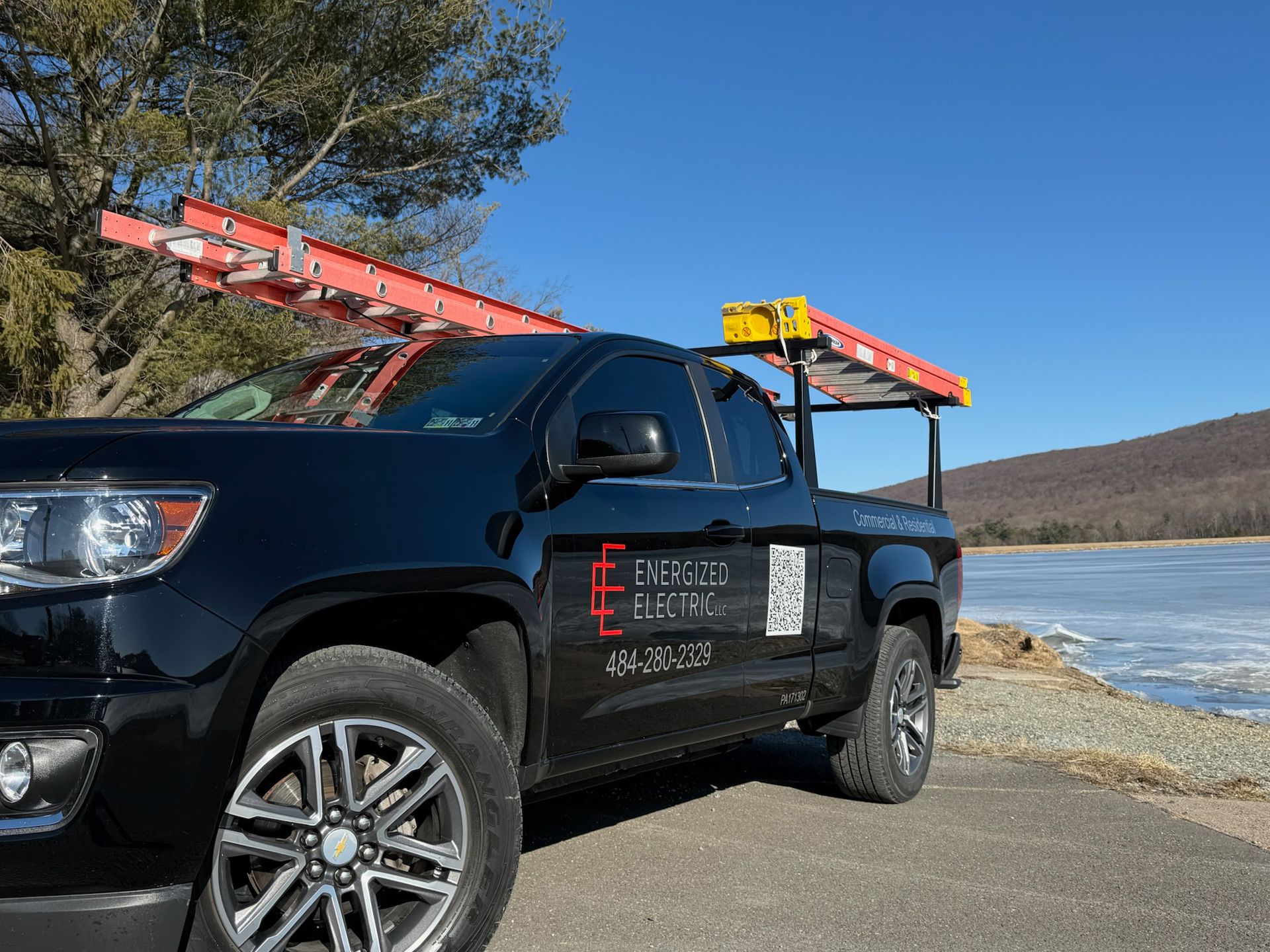 A black truck with a ladder on the back is parked on the side of the road.