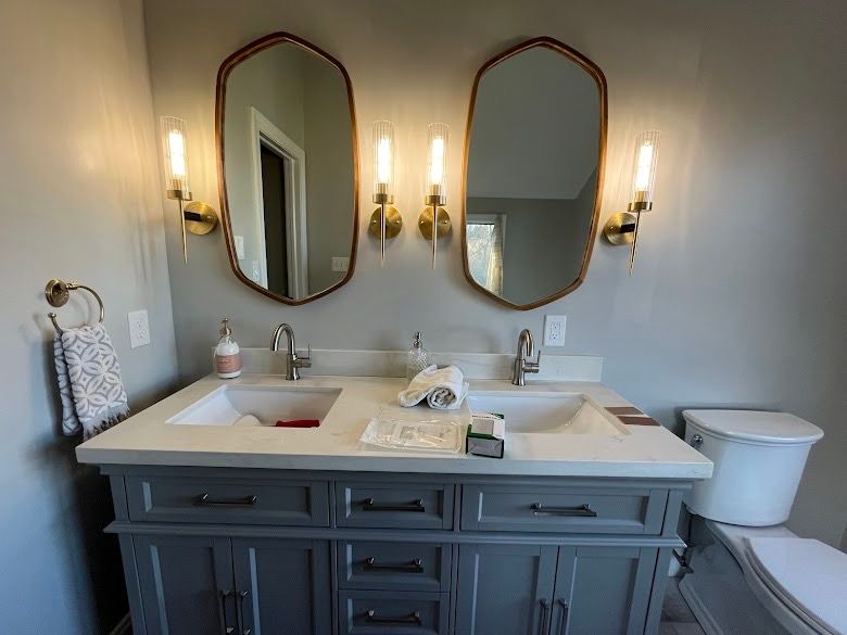 A bathroom with two sinks , two mirrors and a toilet.
