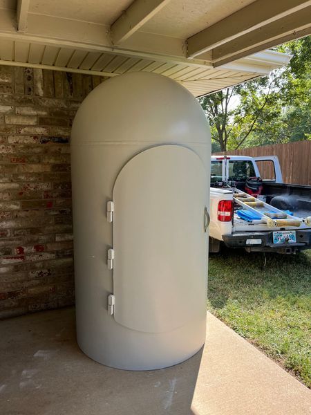 Gray, domed storm shelter on a concrete patio, with a pickup truck in the background.