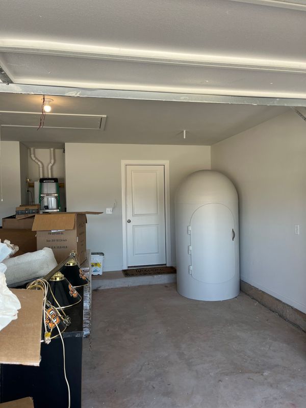 Garage interior with white walls, a closed door, and a white, cylindrical structure.