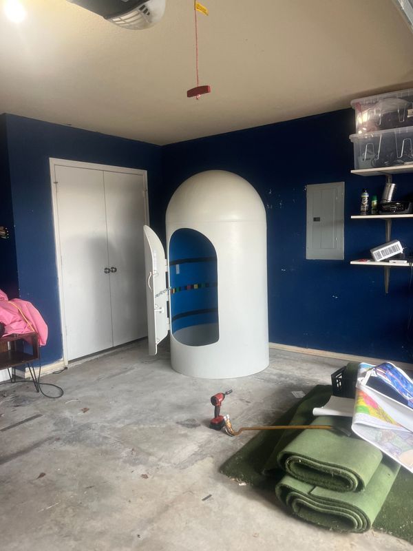 White floatation therapy tank in a garage with blue walls and concrete floor.