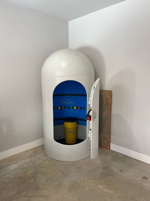 White sensory deprivation tank with open door, yellow bucket inside. Located in a corner.