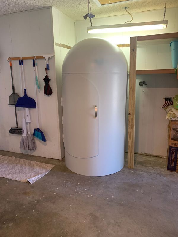 White cylindrical isolation tank inside a garage, next to cleaning tools and shelves.