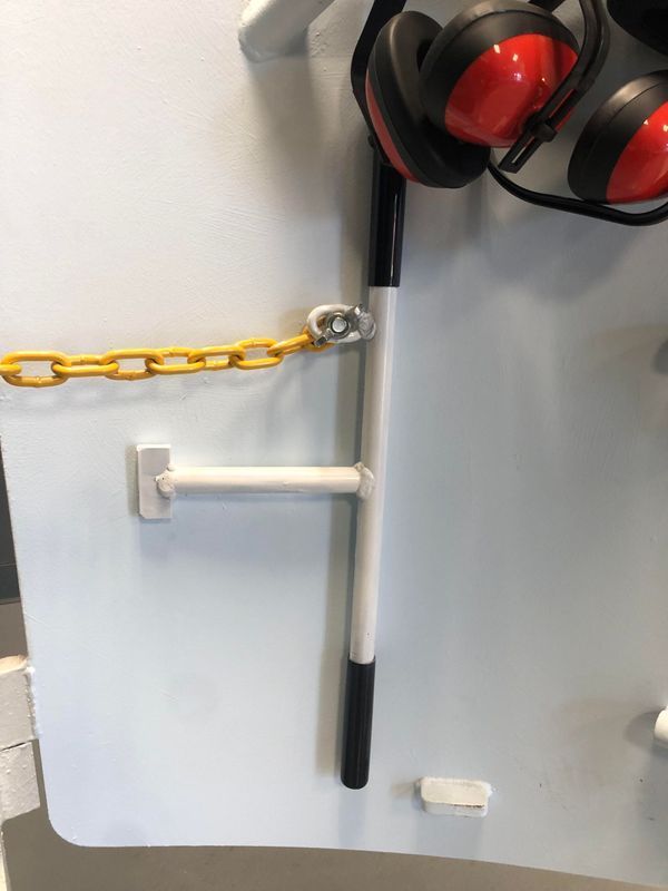 White metal door with a yellow chain, handle, and red earmuffs.