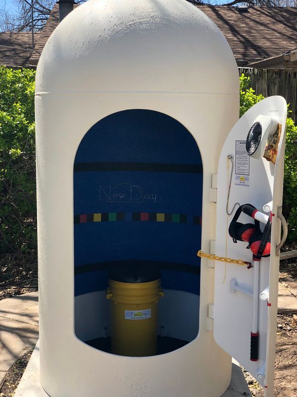 White silo with blue interior, open door revealing a yellow bucket and tools, outdoors.