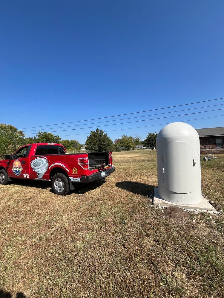Red pickup truck next to a gray utility box on a grassy field under a blue sky.