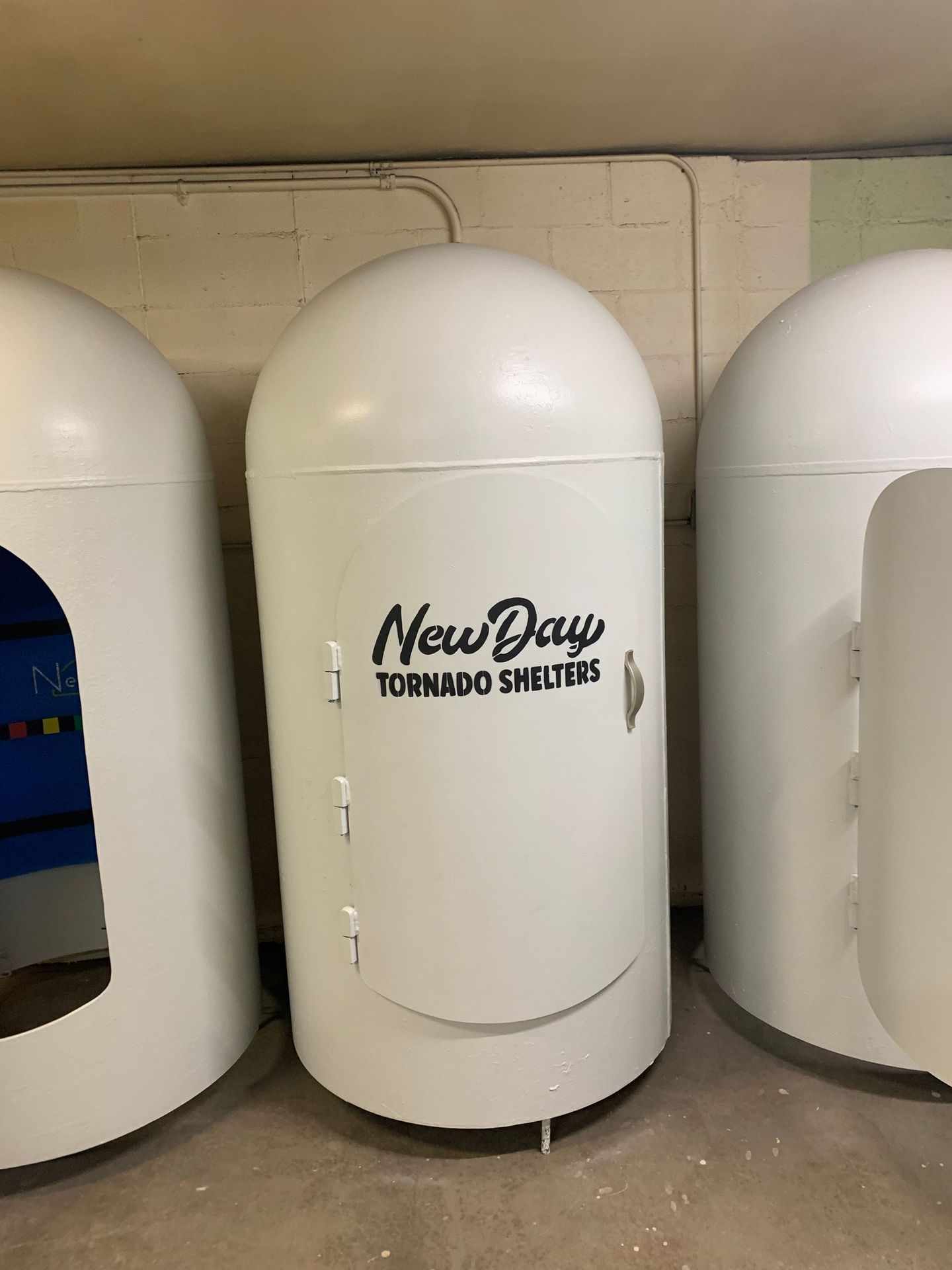 Three white tornado shelters with rounded tops and doors, labeled 