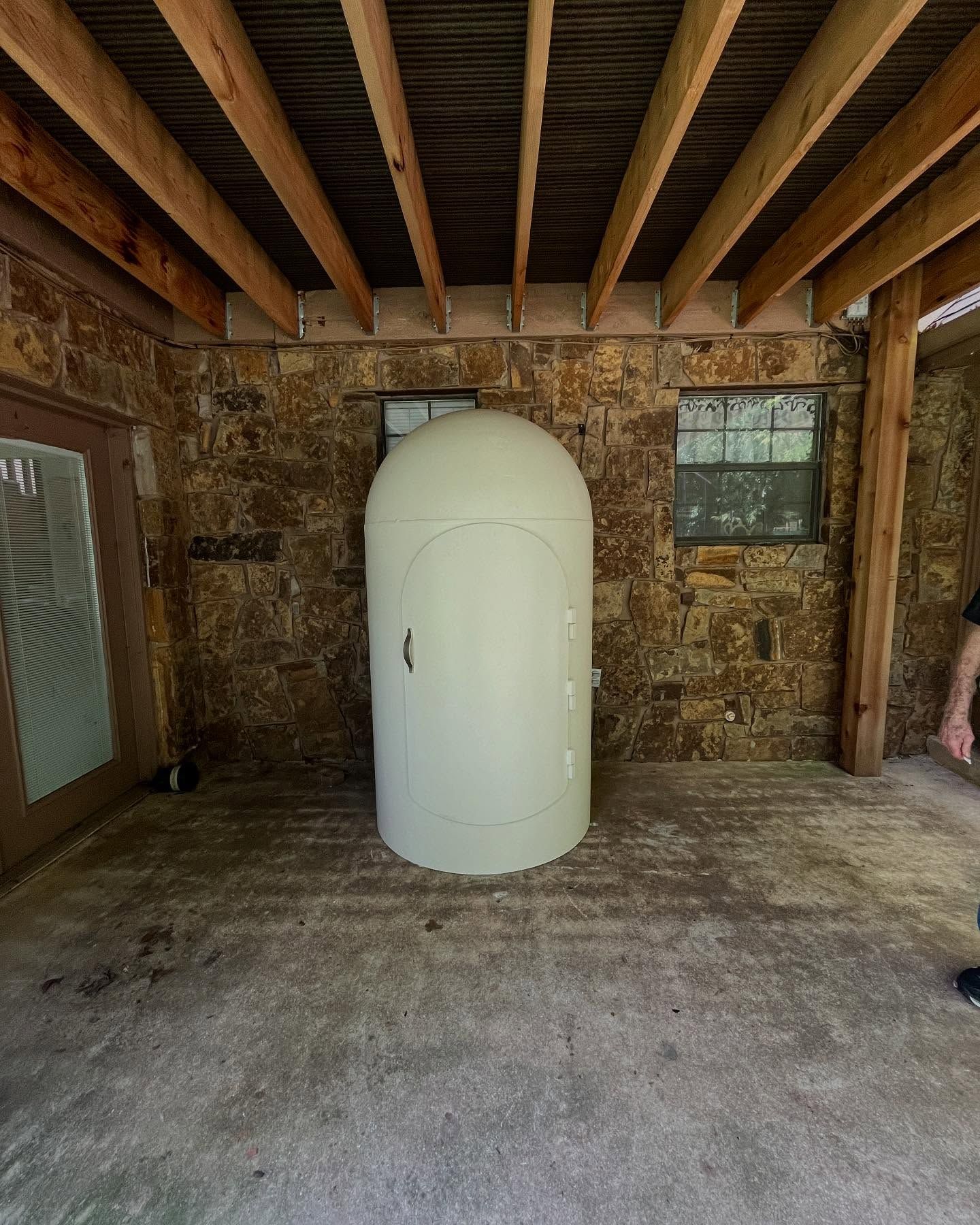 A large, cream-colored, pod-shaped structure on a concrete patio, under a wooden ceiling.