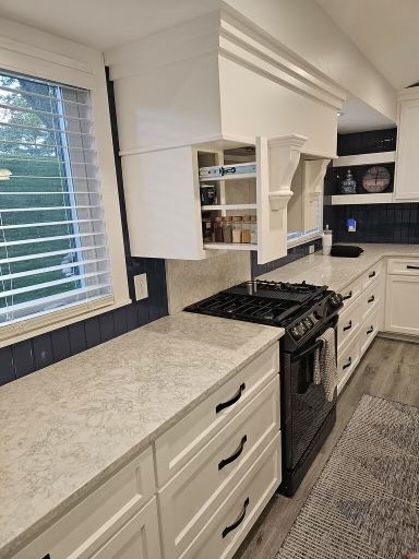 White kitchen with stove, range hood, cabinets, and light countertop. Pull-out spice rack.