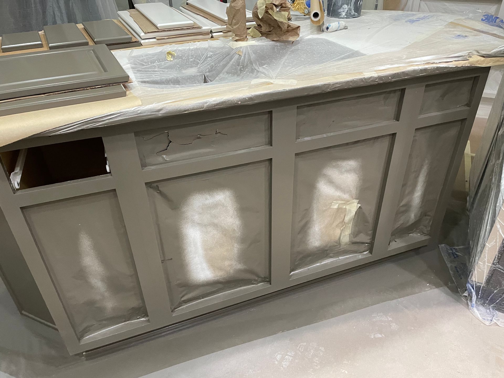 Gray kitchen island during renovation, taped and covered with paint overspray.