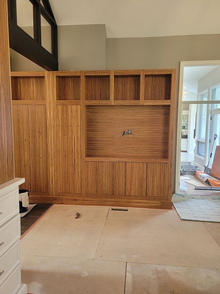 Wooden built-in storage unit with open shelves, cabinets, and a central panel, in a room under construction.