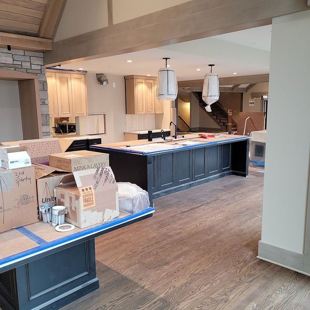 Spacious kitchen with dark island and light wood cabinets, under construction with boxes and tape.