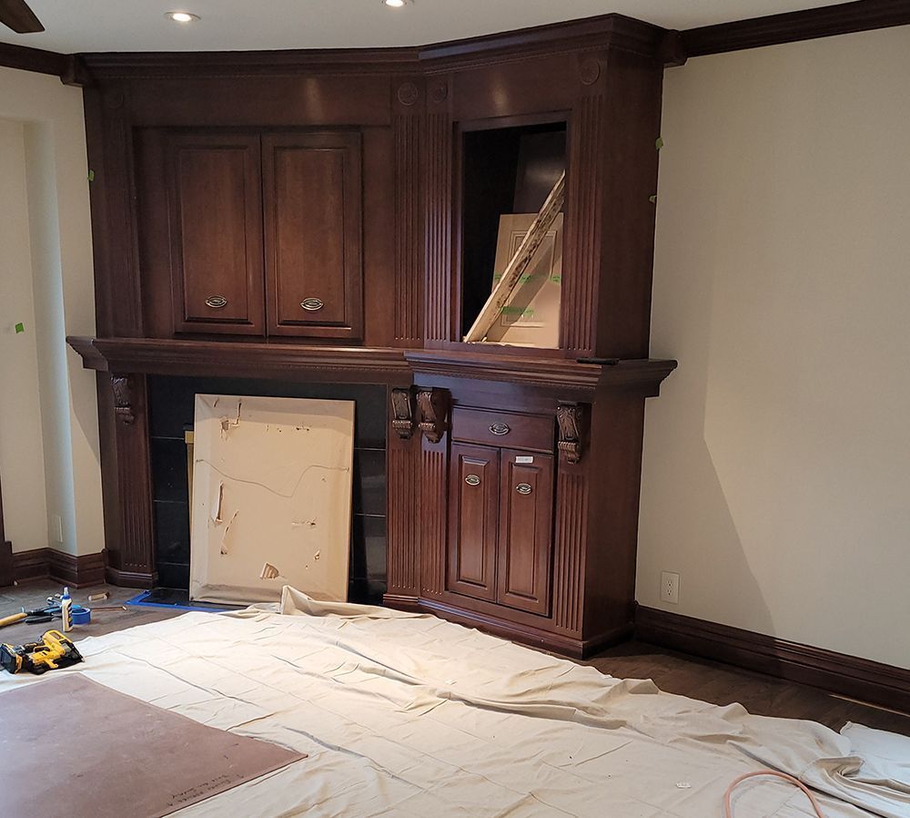 Dark wood built-in cabinet in corner with doors, drawers, and an open shelf. Painting supplies are on the floor.
