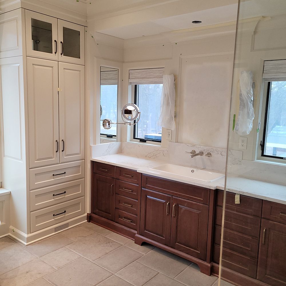 Bathroom with white and brown cabinets, light-colored countertops, tile floor, and large mirror.