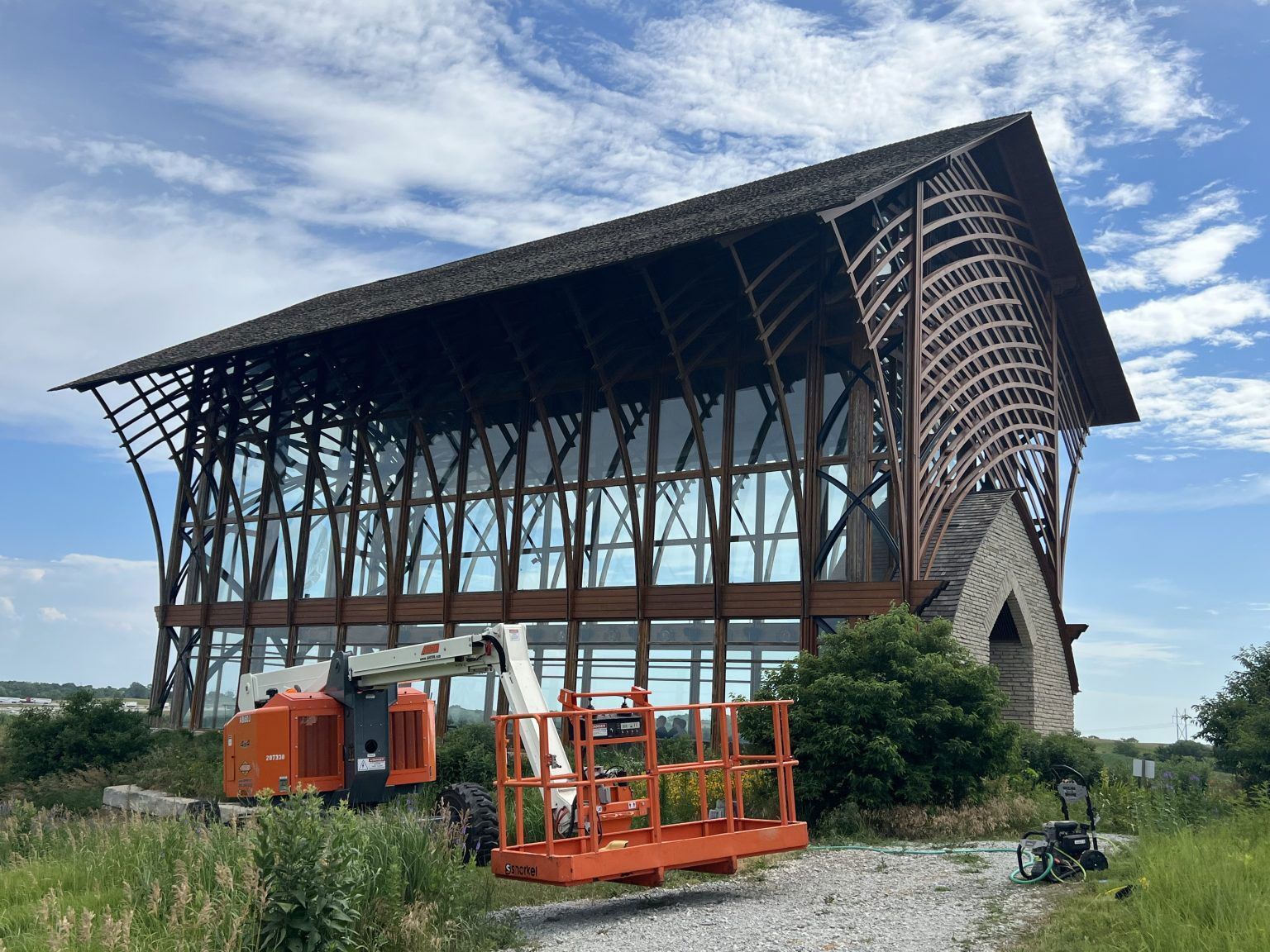 A modern church with brown wooden structure and large glass windows. An orange lift sits in front.