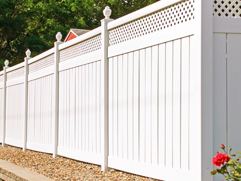 White vinyl privacy fence with lattice top, decorative posts, and red rose.