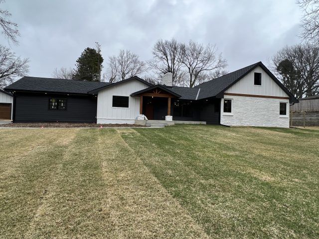 Modern house with black and white exterior, chimney, and grassy lawn on an overcast day.