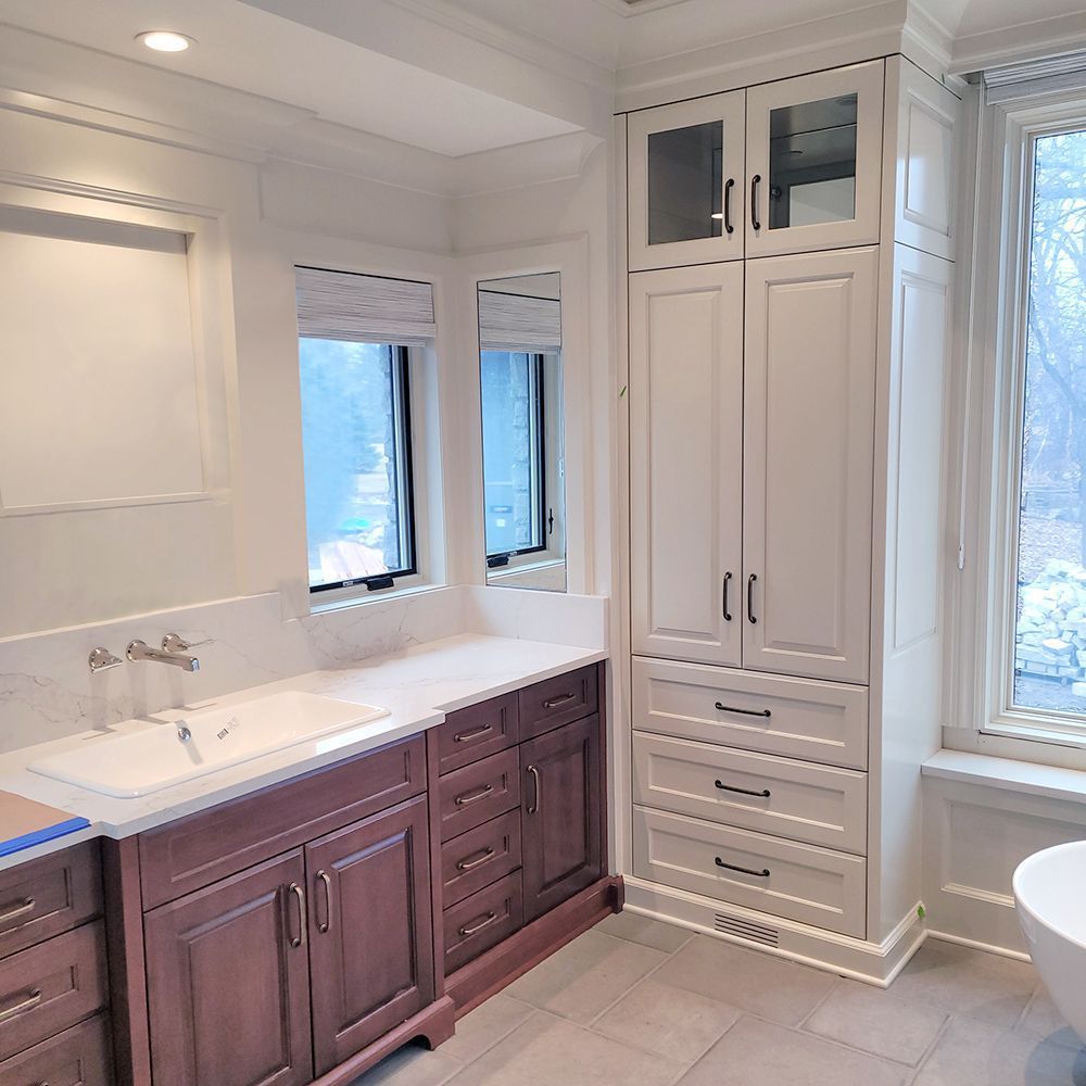 Bathroom with white and brown cabinets, sink, and window.