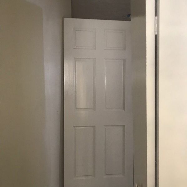 White six-panel door standing in a hallway. The door is slightly ajar.