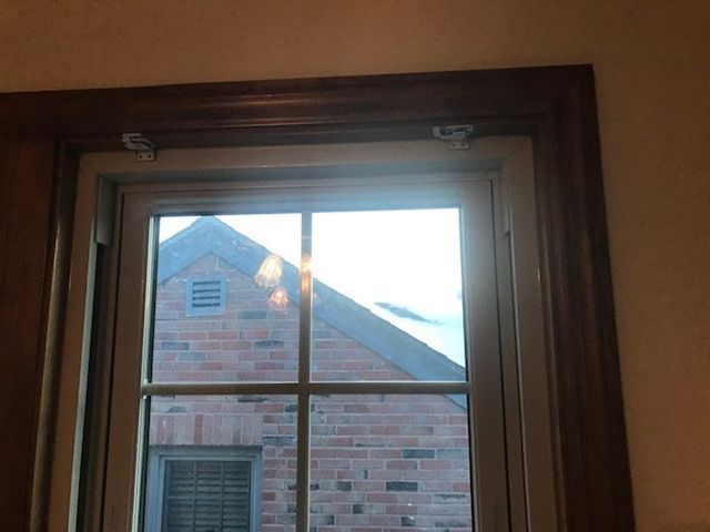 Window with wooden trim, looking out onto a brick building with a triangular roof.