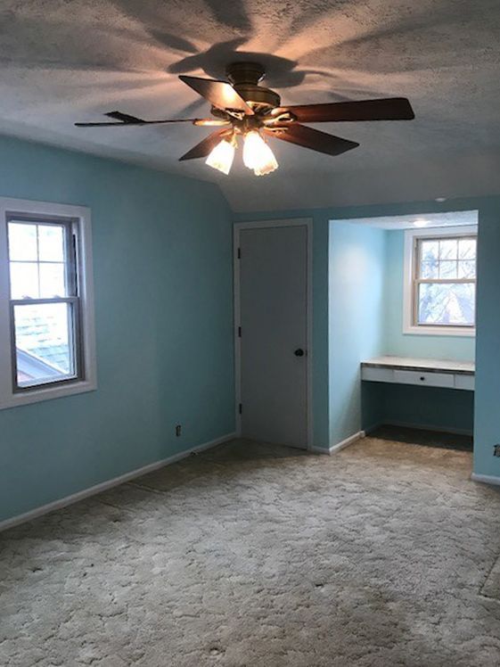 Bedroom with blue walls, carpet, and a ceiling fan. Includes a door, two windows, and a built-in desk.