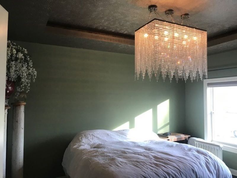 Bedroom with a green wall, white bed, large crystal chandelier, and a window.