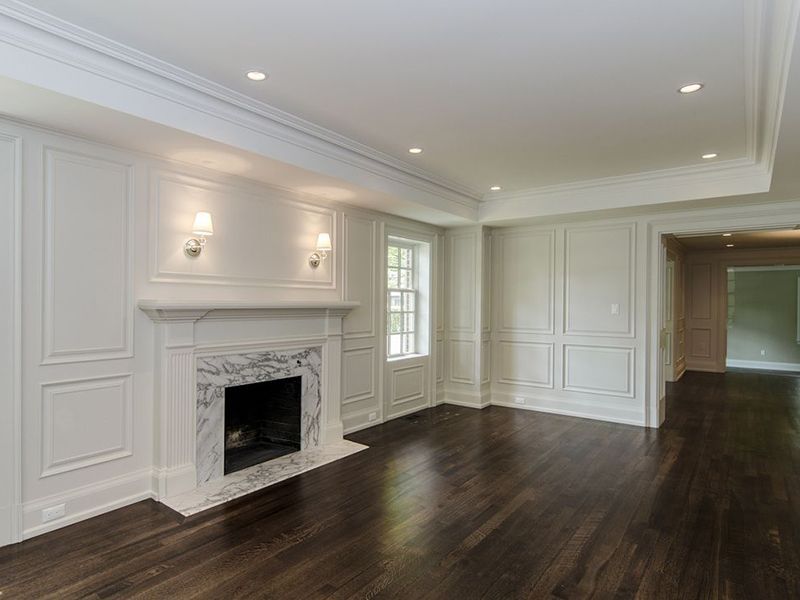Empty living room with dark hardwood floors, white walls, fireplace, and recessed lighting.