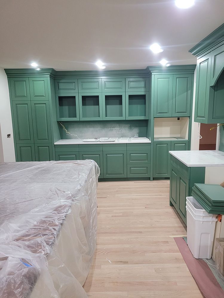 Green kitchen cabinets with white countertops, wooden floors, and an island covered in plastic.