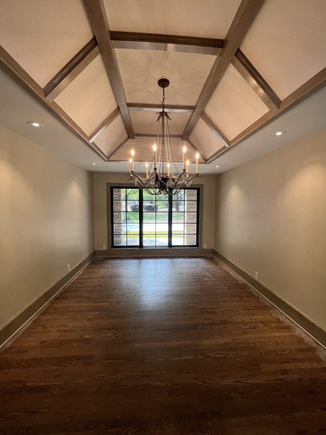 Empty dining room with dark wood floor, chandelier, and a beamed ceiling.