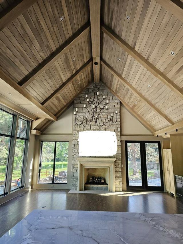 Vaulted ceiling living room with fireplace and chandelier, large windows, wood floors.