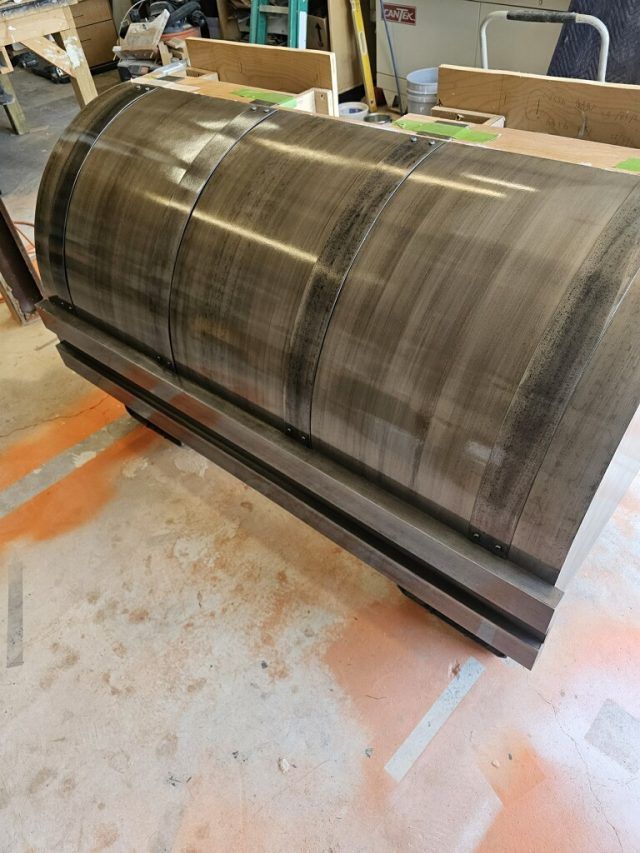 Dark brown curved wooden chest in a workshop, sitting on a concrete floor.
