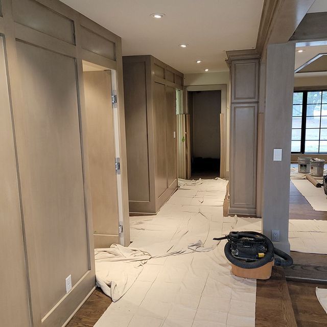 Hallway with beige cabinetry and doors, floor covered with drop cloths, vacuum cleaner on floor.